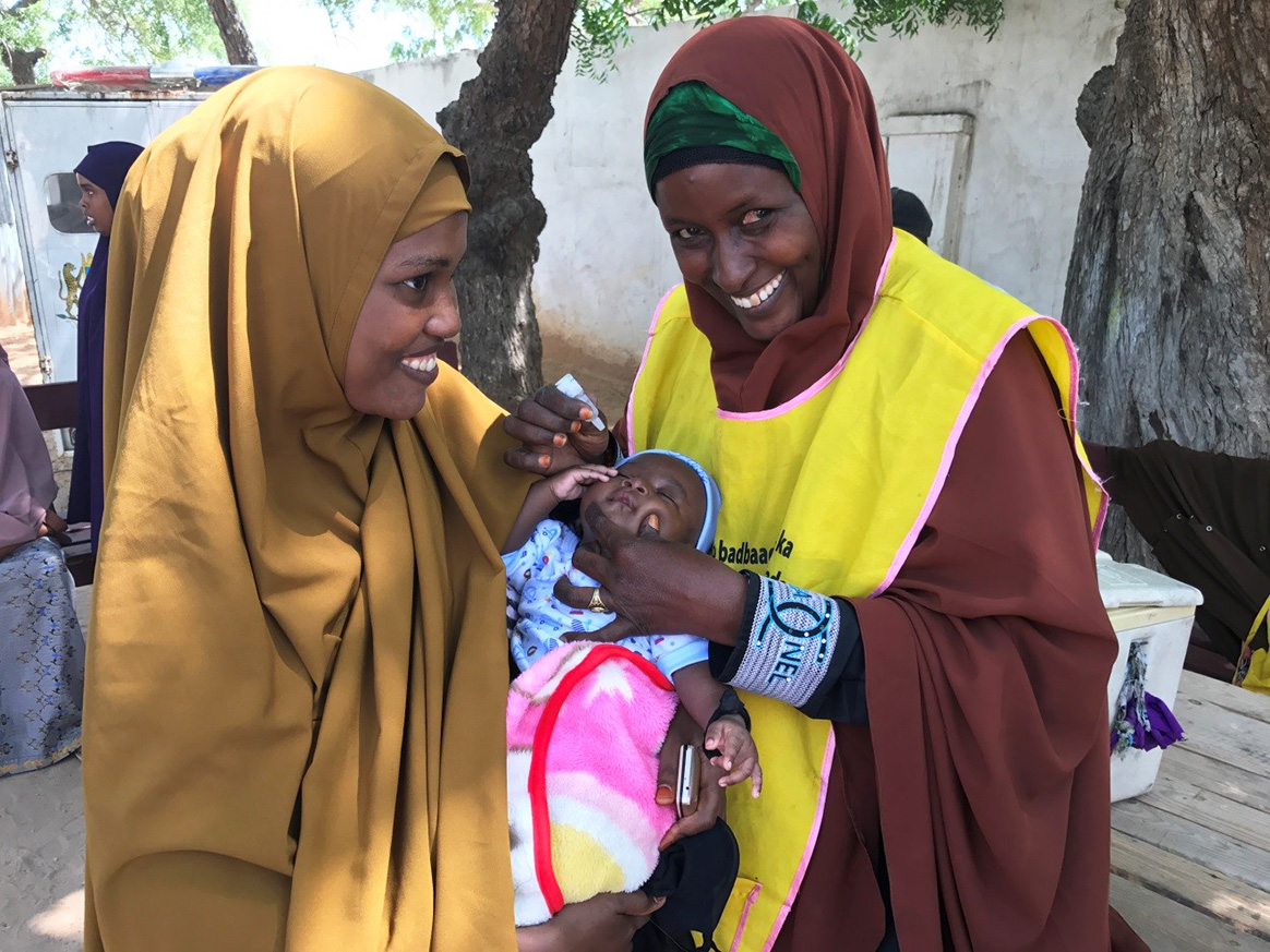 Bella smiles as she vaccinates a small baby against polio – one of hundreds of children she will protect over the course of a campaign. © WHO Somalia