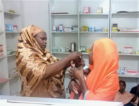 Halima administers the oral polio vaccine to a child at a pharmacy where she works as a polio surveillance focal point. © WHO Nigeria