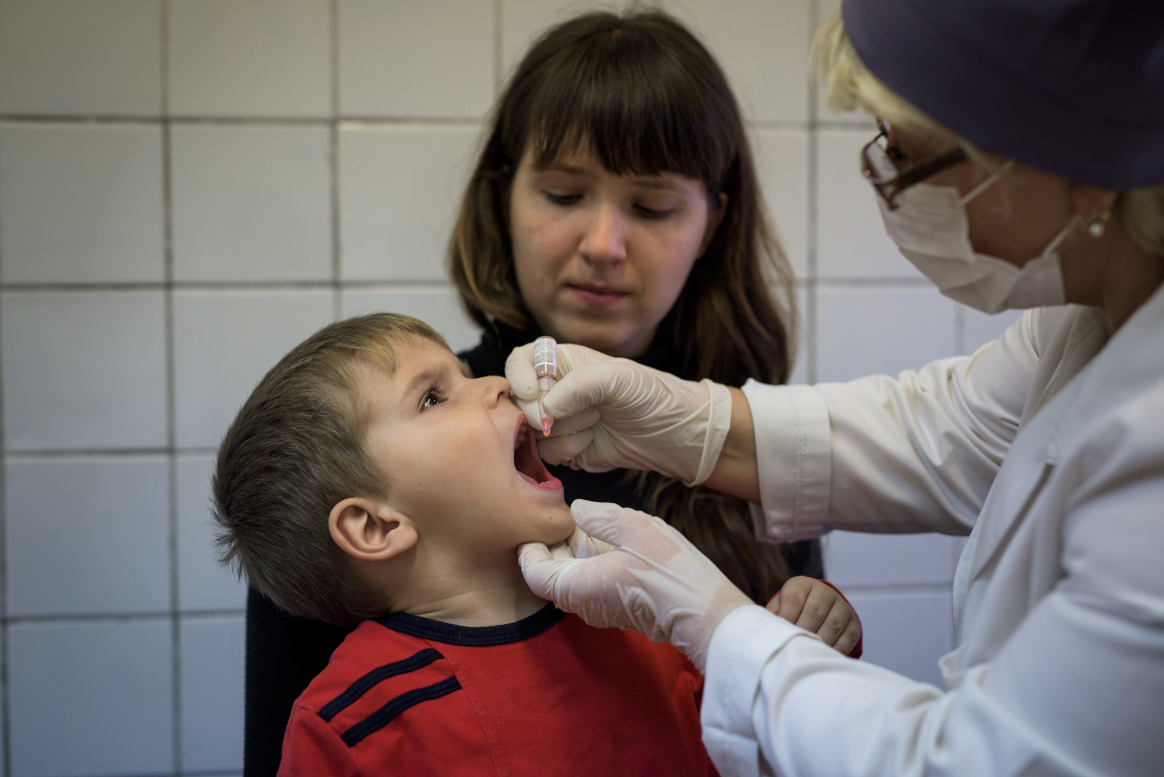 Boy receiving polio drops from a health worker, with his mother during a polio vaccination campaign in 2015. © WHO / Alex Shpigunov