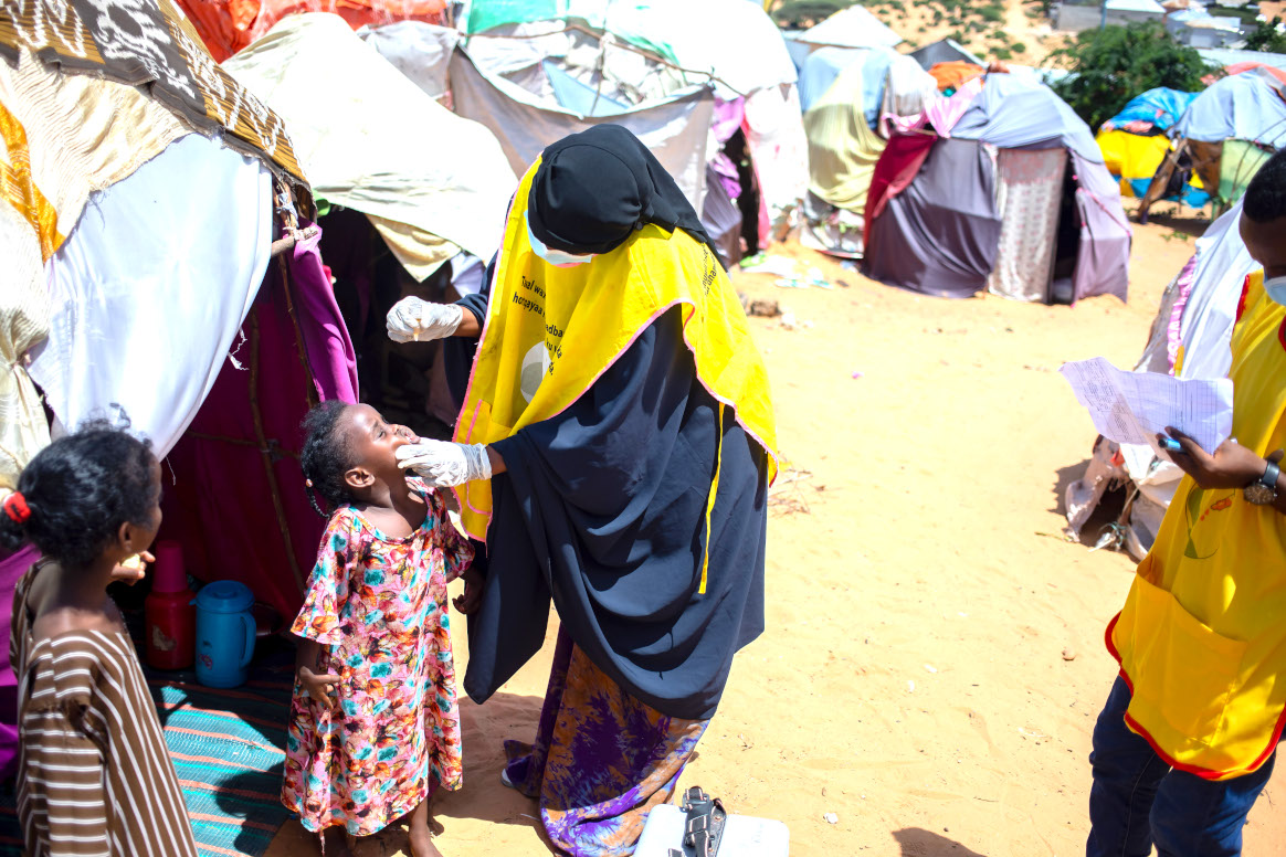 A health worker administers polio vaccine (nOPV2) drops to a child at Luley IDP camp during a door-to-door polio immunization campaign in Kahda district, Mogadishu, Somalia on May 28, 2023. © Ismail Taxta/Getty Images