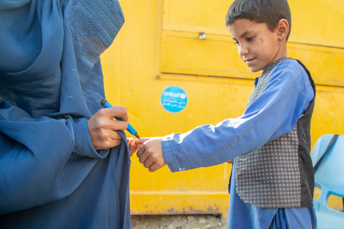 At a temporary health facility in Eastern Afghanistan, near the Torkham border crossing point with Pakistan, a female mobiliser vaccinator marks the finger after administering the polio vaccine to an Afghan boy who has recently returned from Pakistan. © UNICEF/UNI530950/Karimi
